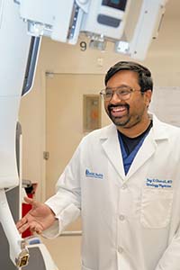 A man in a white doctor's coat smiles as he looks off camera.