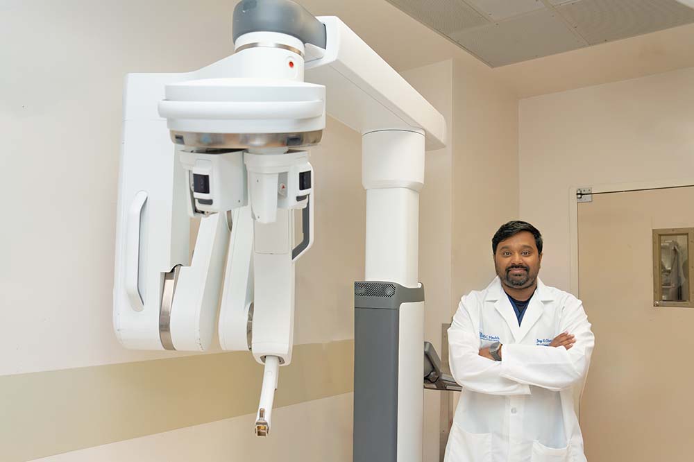 Man in white doctor's coat stands beside a large white surgical system.