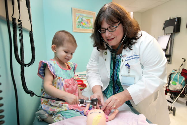 Dr. Jacqueline Kraveka and child assistant examine a doll.