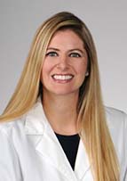 Woman smiling for a headshot wearing a white doctor's coat.