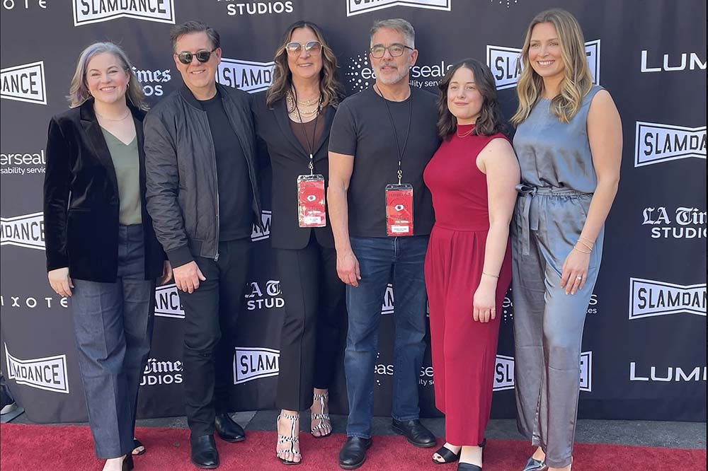 Six people pose against a backdrop with the word Slamdance on it.