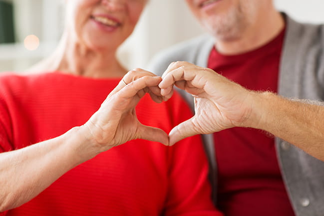 A pair of adults each creating one half of a heart sign with their hands.