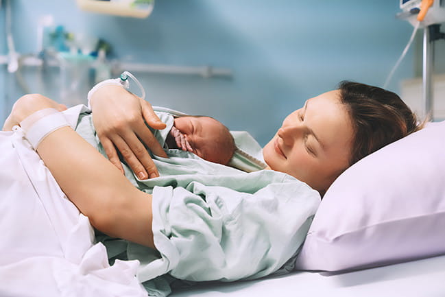A woman in a hospital bed smiles as she holds her newborn baby.