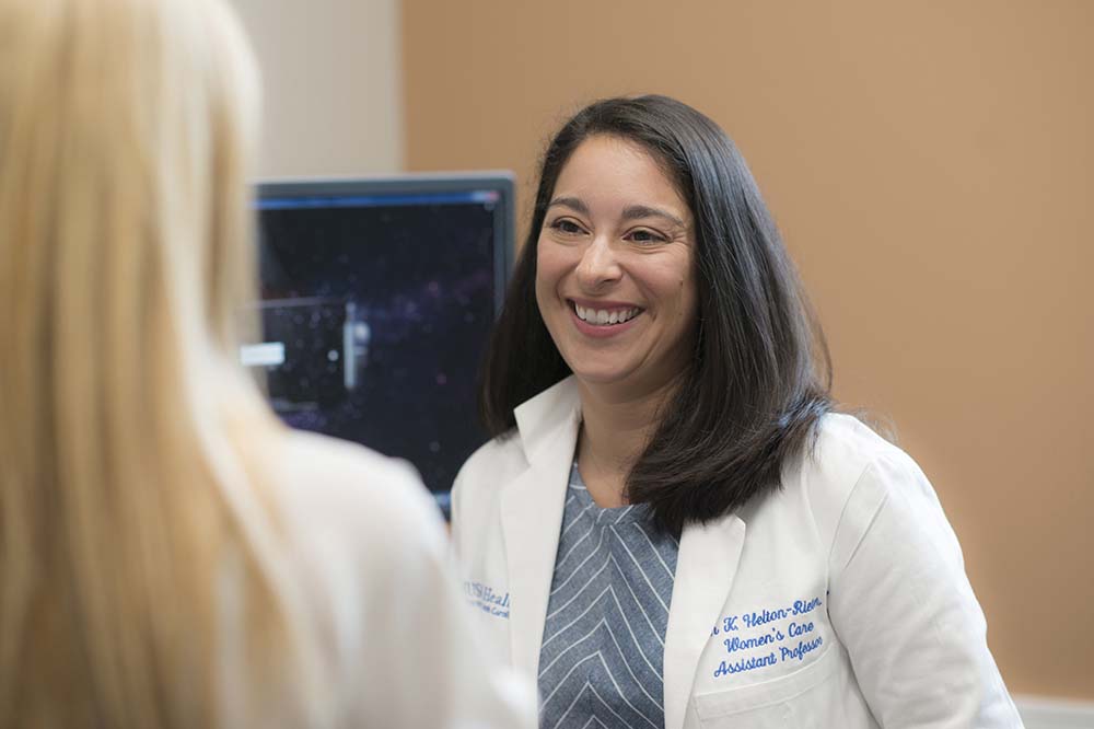 Woman in white doctor's coat talks with another woman whose back is to the camera.